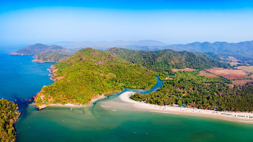 A coastal landscape with a river flowing into the sea, surrounded by green hills and a beach with umbrellas.