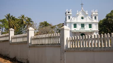A white church with a cross on top, surrounded by a white picket fence and palm trees.