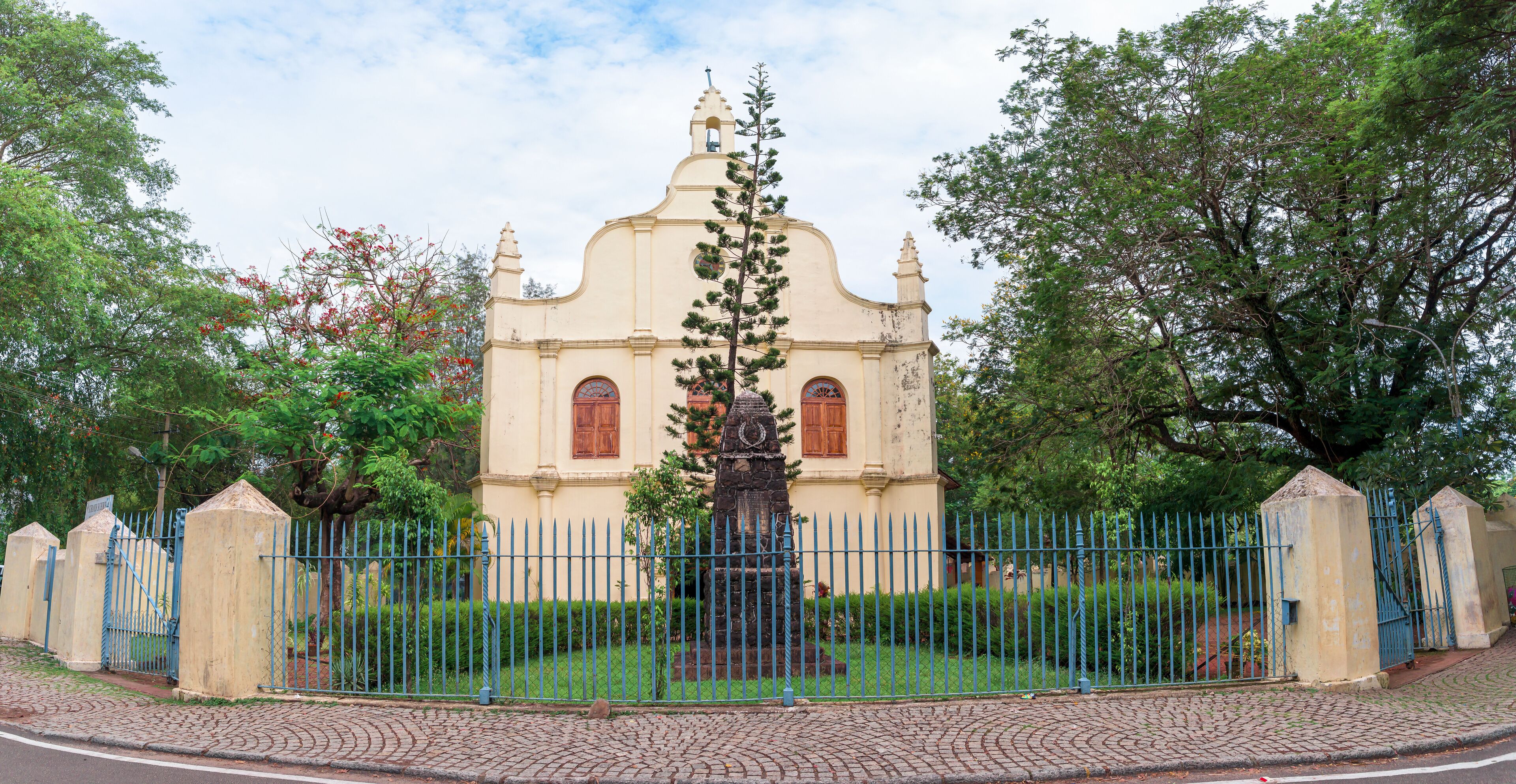 A historic church with a statue in front, surrounded by a blue fence and lush greenery.