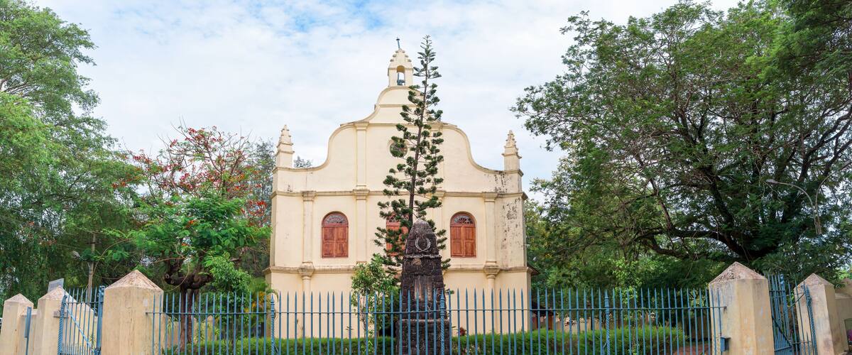 A historic church with a statue in front, surrounded by a blue fence and lush greenery.