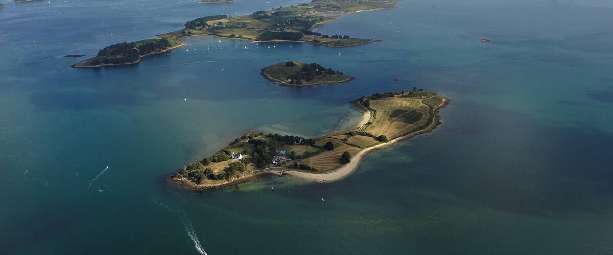 An aerial view of a coastal archipelago with clear waters, small islands, and a few boats.