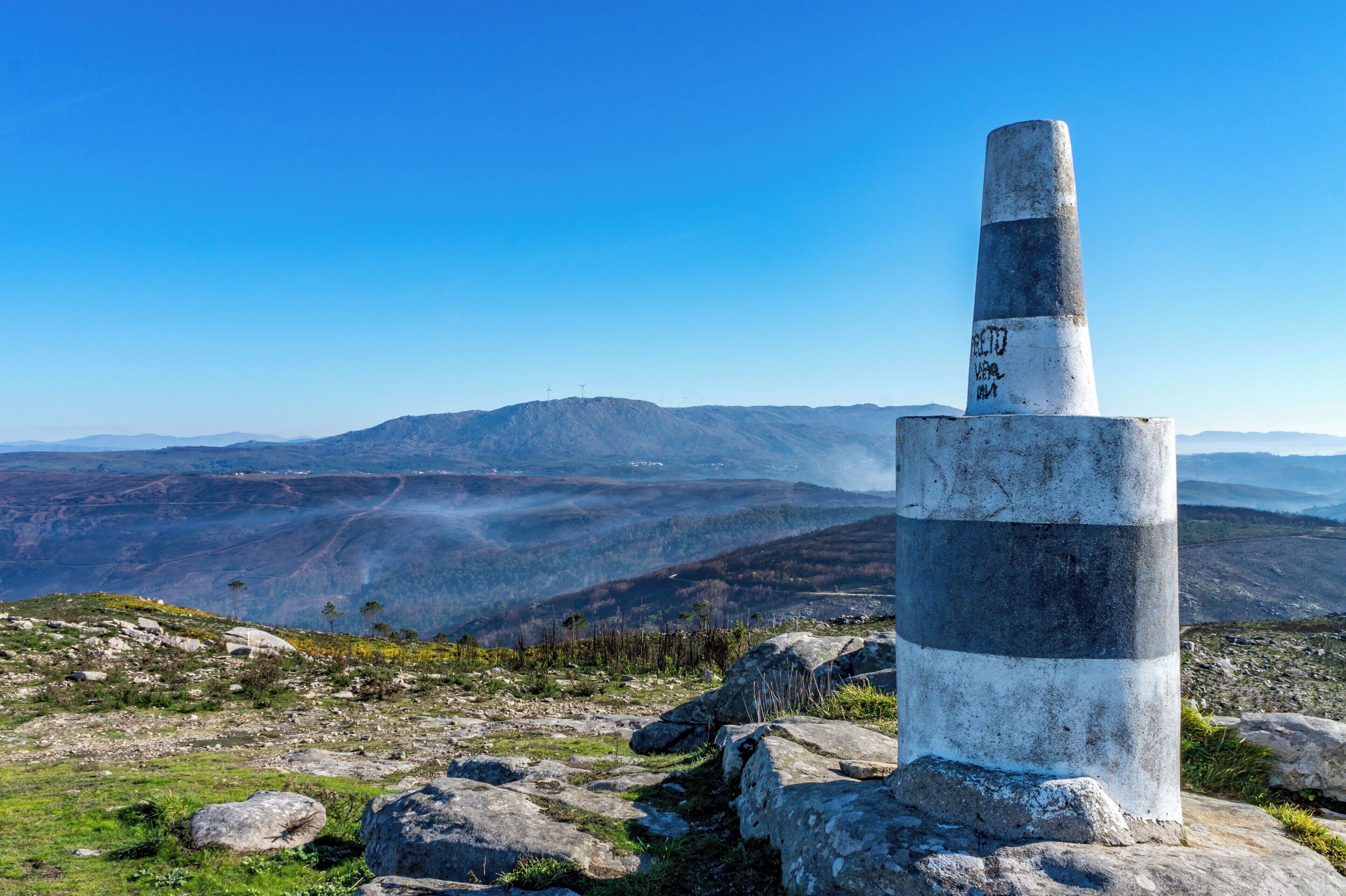 A tall, striped monument on a rocky hill with a panoramic view of mountains and valleys.