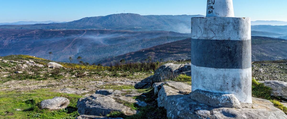 A tall, striped monument on a rocky hill with a panoramic view of mountains and valleys.