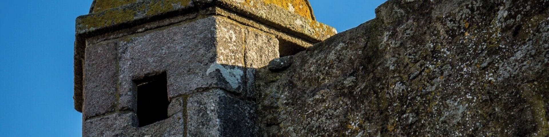 A stone tower with a rounded dome and a spherical finial against a clear blue sky.