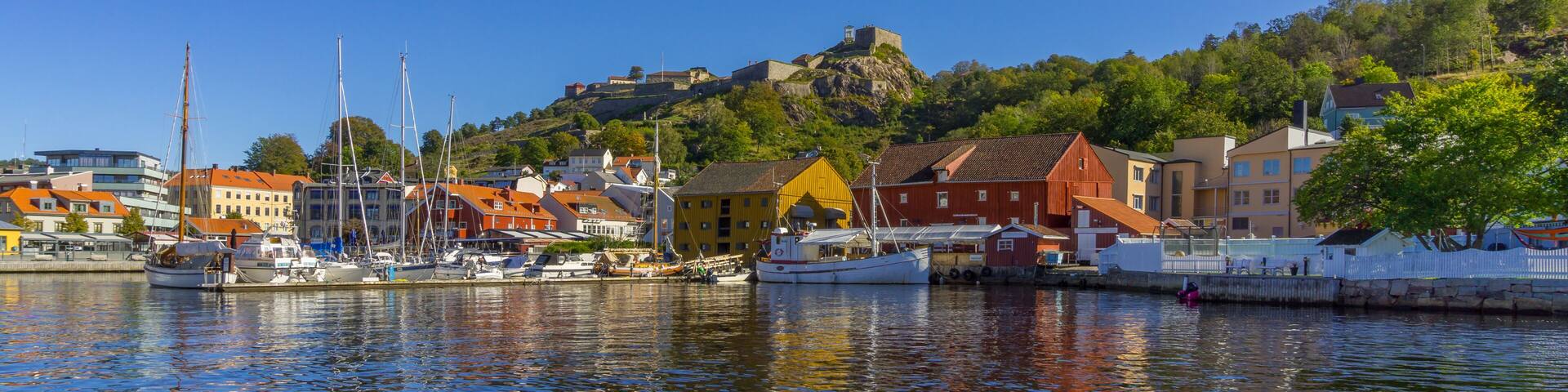 A harbor with boats, colorful buildings, and a hill with a fort.