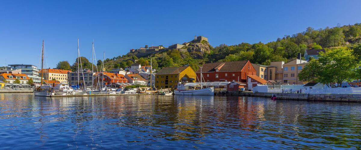 A harbor with boats, colorful buildings, and a hill with a fort.