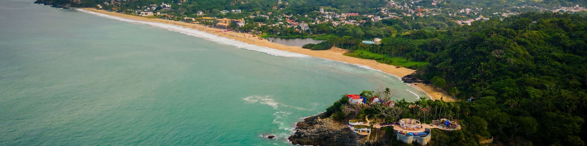 A coastal landscape with a beach, a small island with buildings, and a mountainous backdrop.