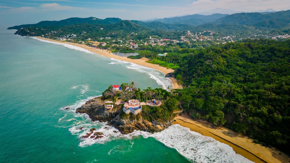A coastal landscape with a beach, rocky outcrops, and a forested area.
