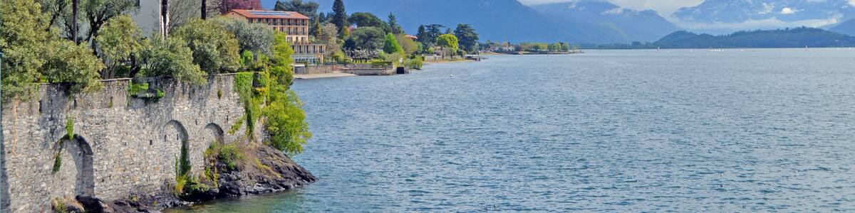 A coastal town with a historic building, a stone wall, and a mountain range in the background.