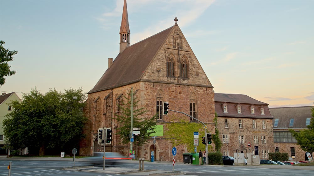 Eine historische Kirche mit einem hohen Turm und ein Gebäude aus Stein mit spitzer Dachform.