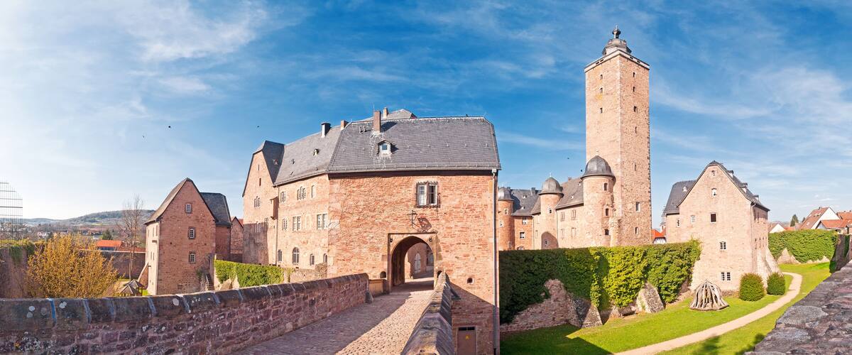A historic castle with a prominent tower, a paved entrance, and surrounding greenery.