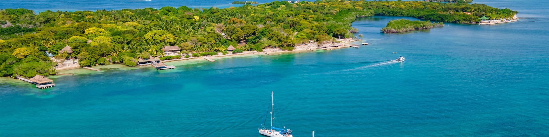 An aerial view of a tropical island with clear turquoise waters, two sailboats, and lush greenery.