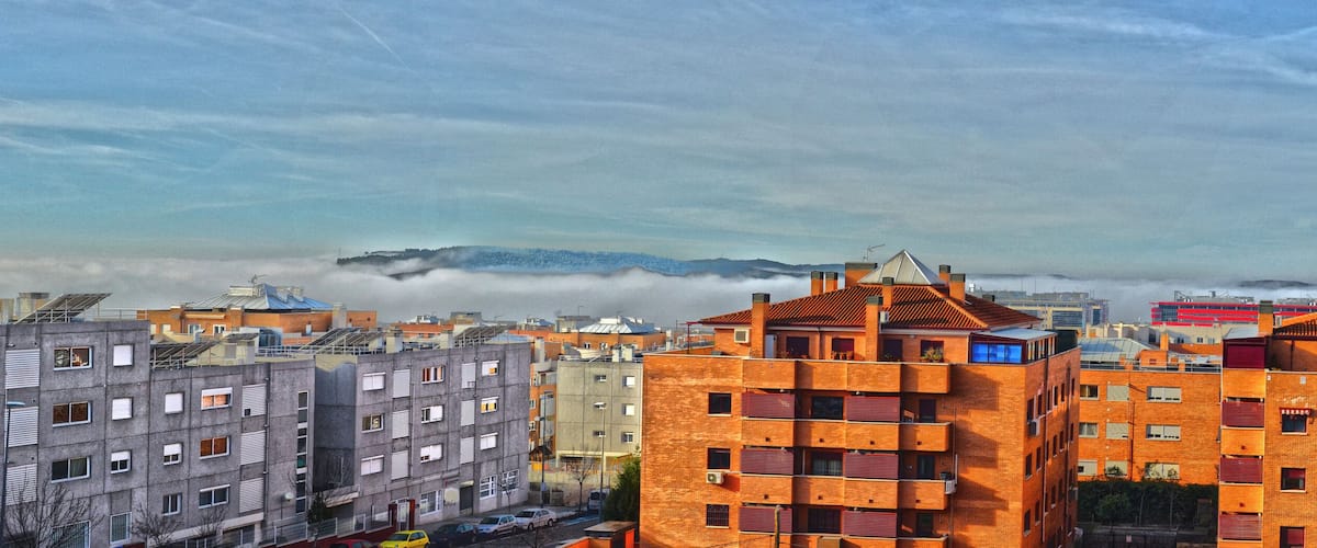 A cityscape with modern and traditional buildings, a cloudy sky, and a distant mountain range.