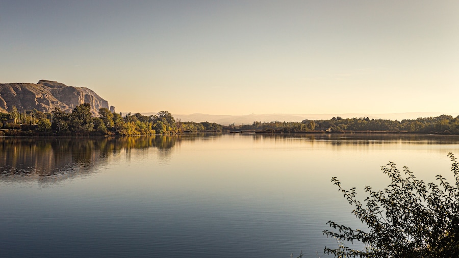 A calm river with a mountain in the background and trees along the riverbank.