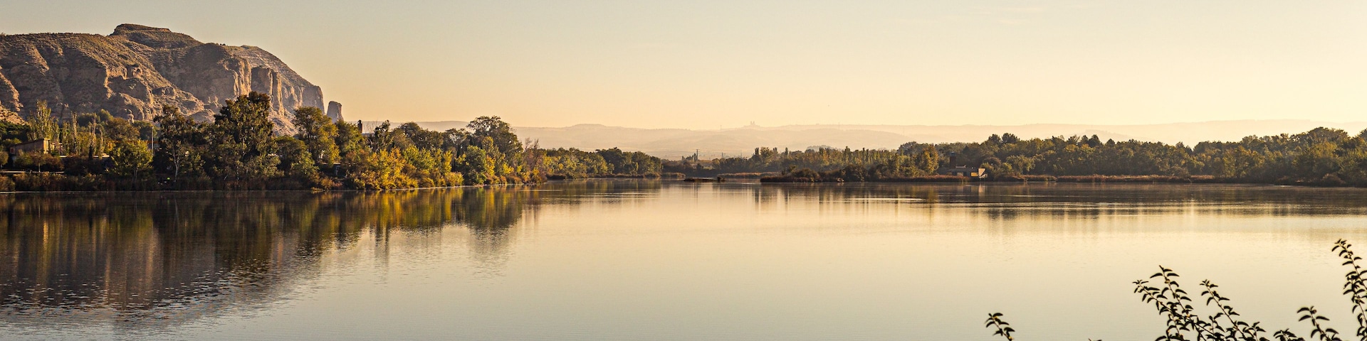 A calm river with a mountain in the background and trees along the riverbank.