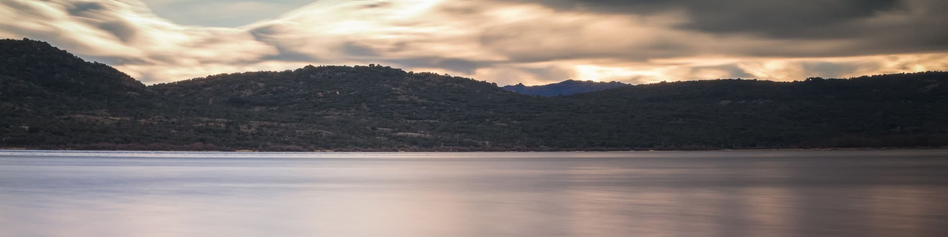 A calm lake with a rocky shoreline and hills in the background.