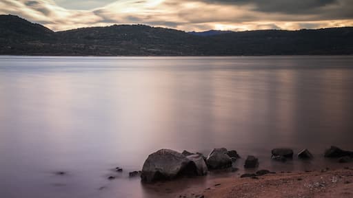 A calm lake with a rocky shoreline and hills in the background.