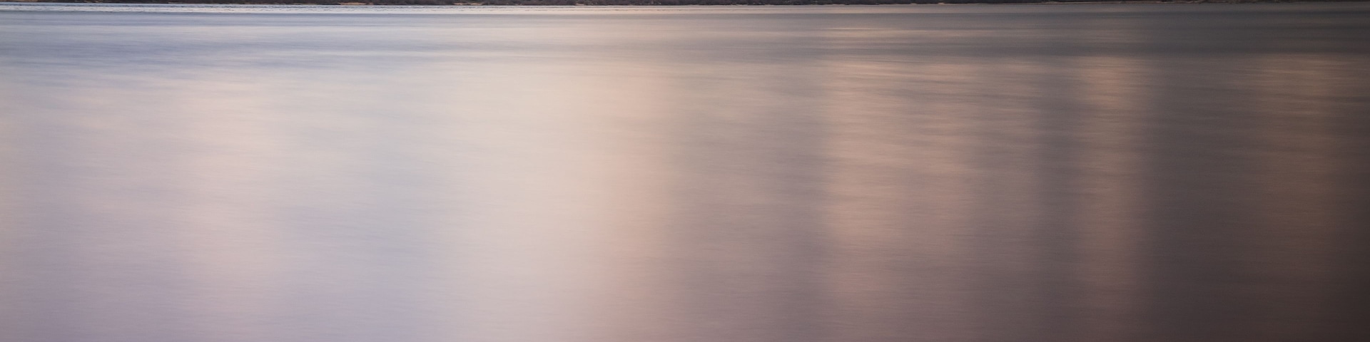 A calm lake with a rocky shoreline and hills in the background.