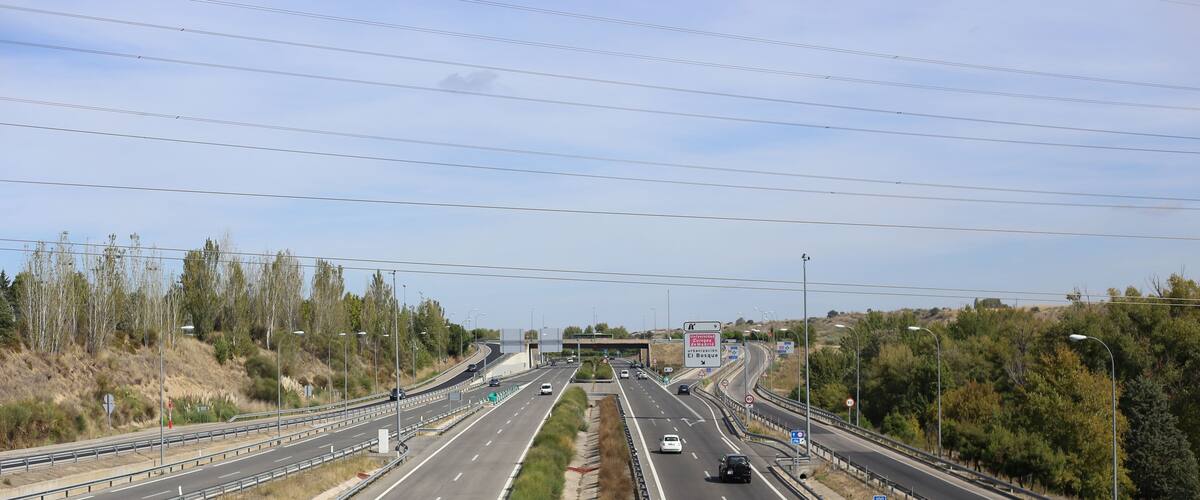 A multi-lane highway with a central divider, guardrails, and sparse vegetation.