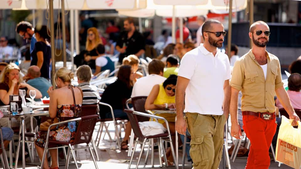 A crowded outdoor dining area with metal chairs and tables, people sitting and walking.