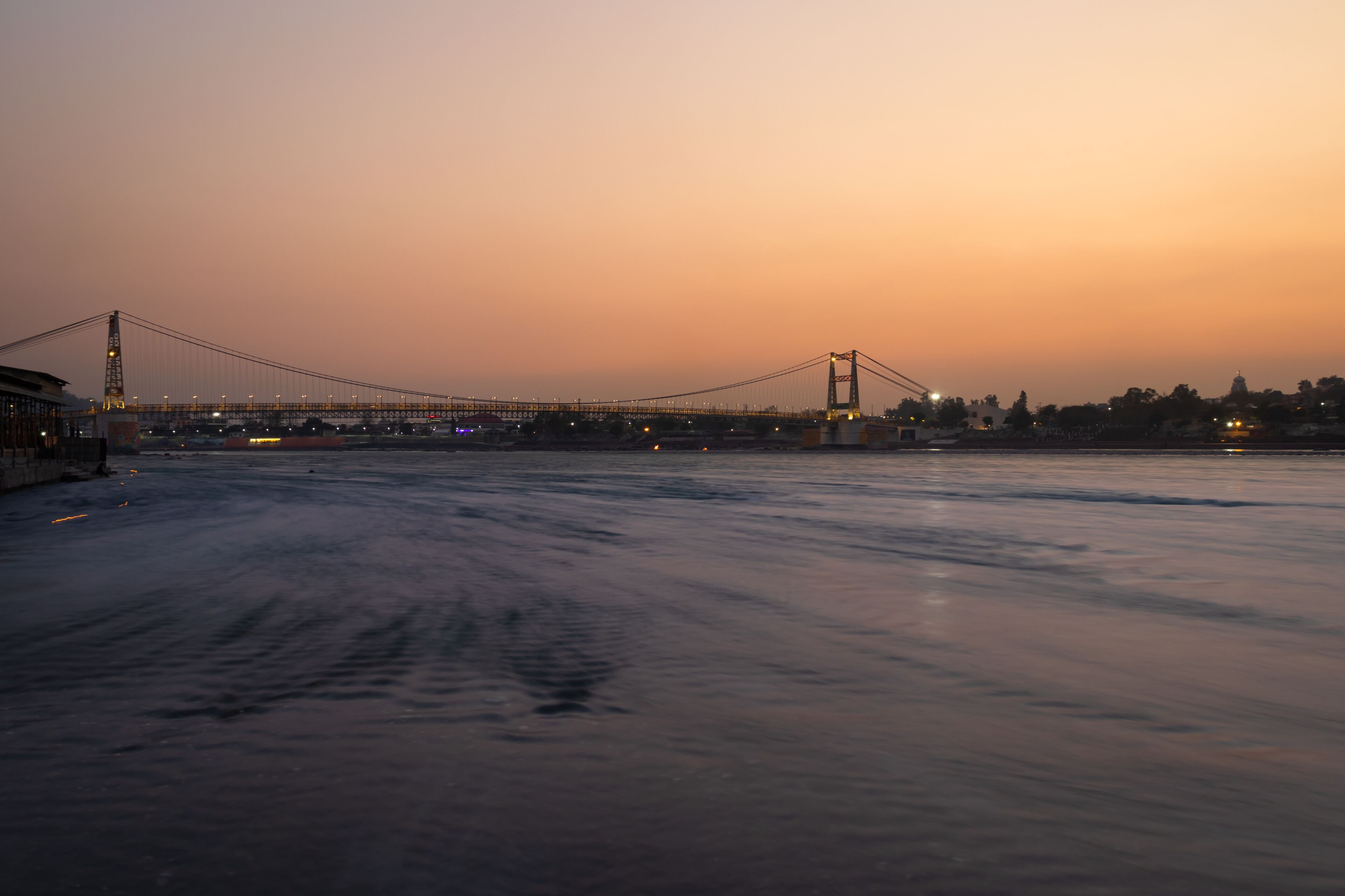 A bridge spanning a river at dusk with city lights in the background.