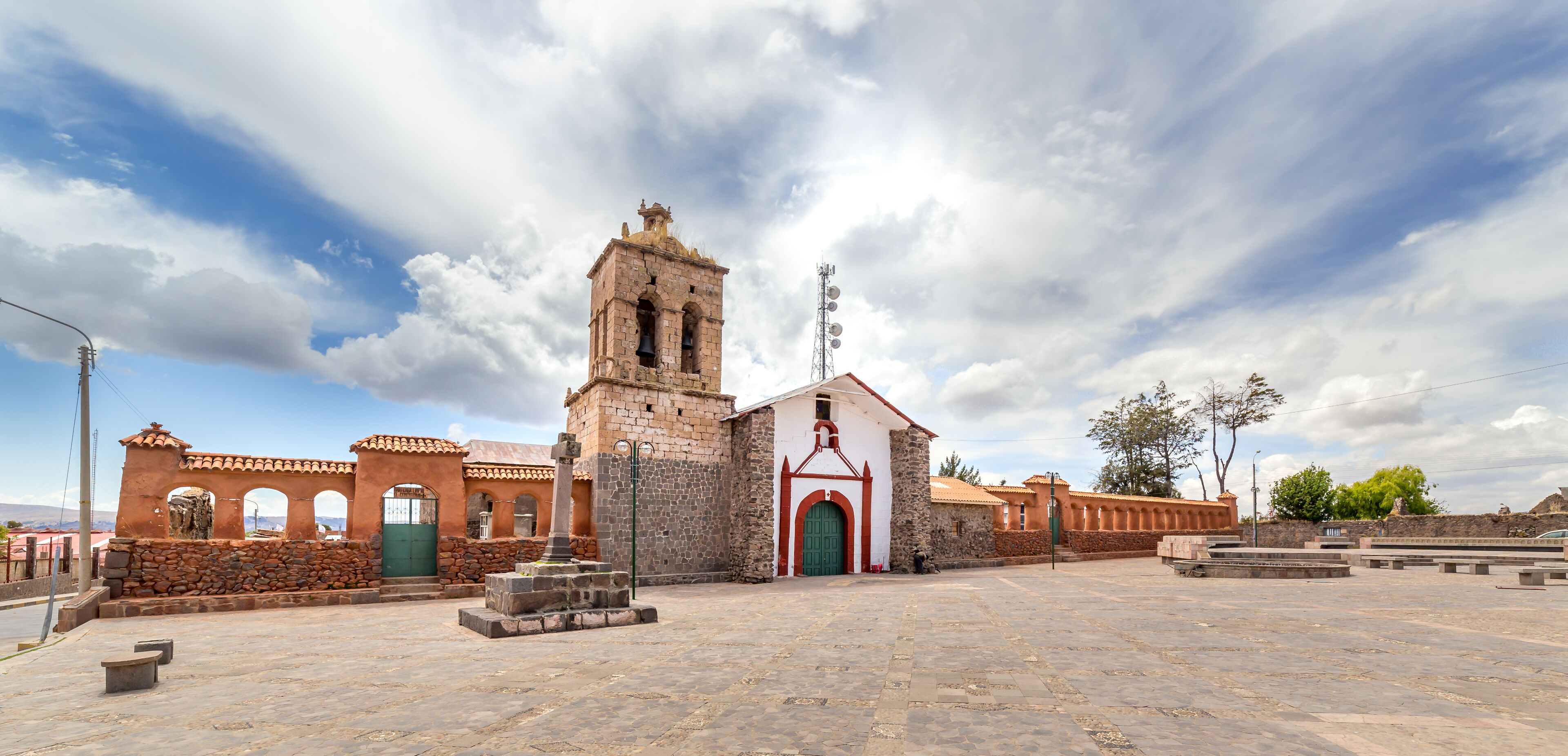 A historic church with a bell tower, a stone wall, and a plaza with benches.