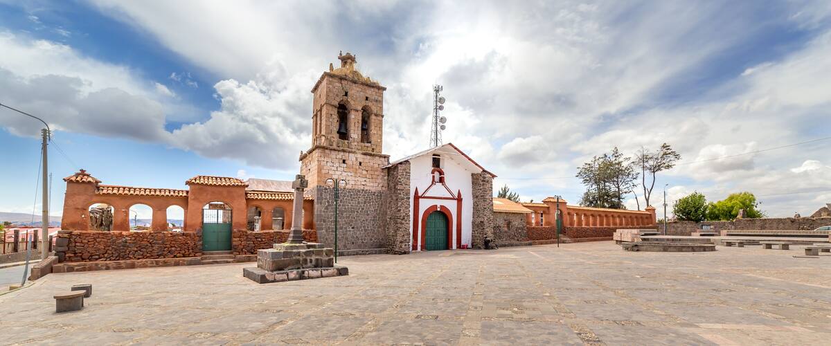 A historic church with a bell tower, a stone wall, and a plaza with benches.