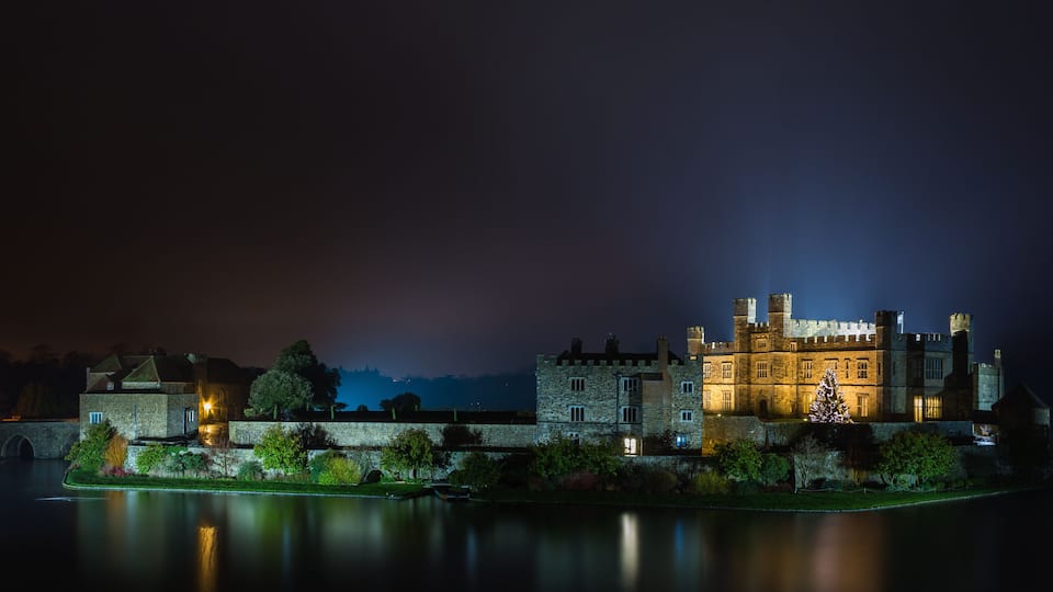 A historic castle by a calm river at night.