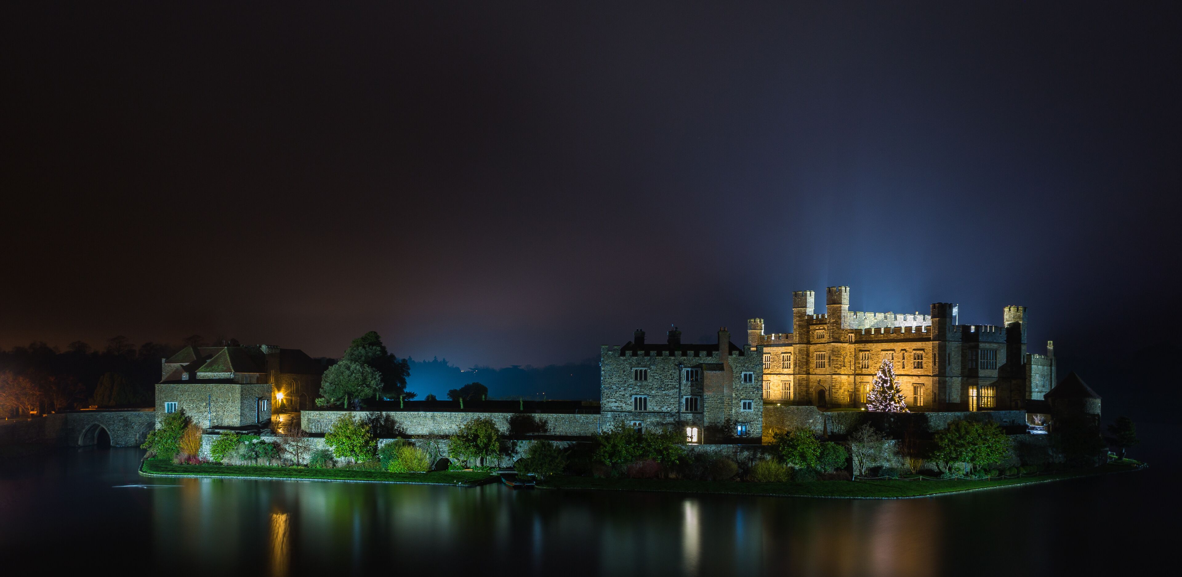 A historic castle by a calm river at night.