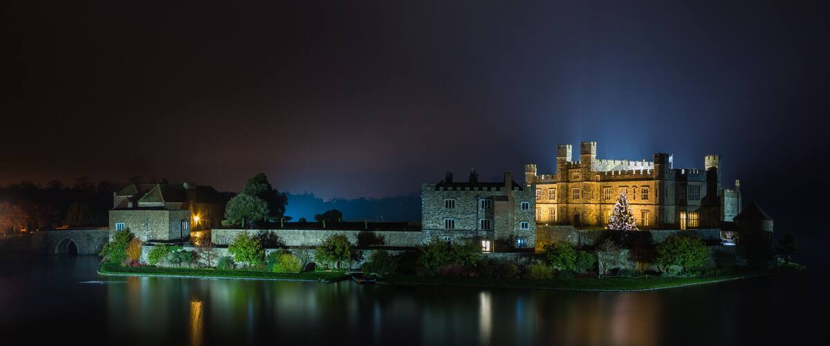 A historic castle by a calm river at night.