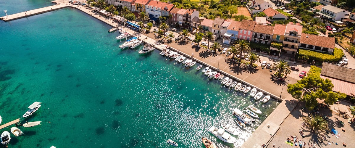 A coastal town with a marina, houses, and a mountainous backdrop.