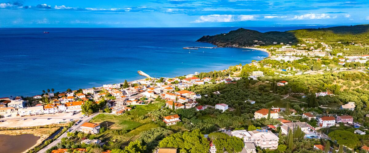 A coastal town with a beach, houses, and a mountainous backdrop.