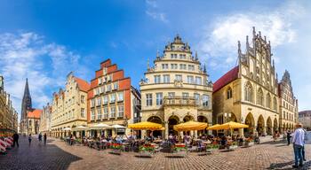 Ein historischer Platz mit prunkvollen Gebäuden, Straßencafés und einem markanten Kirchturm.