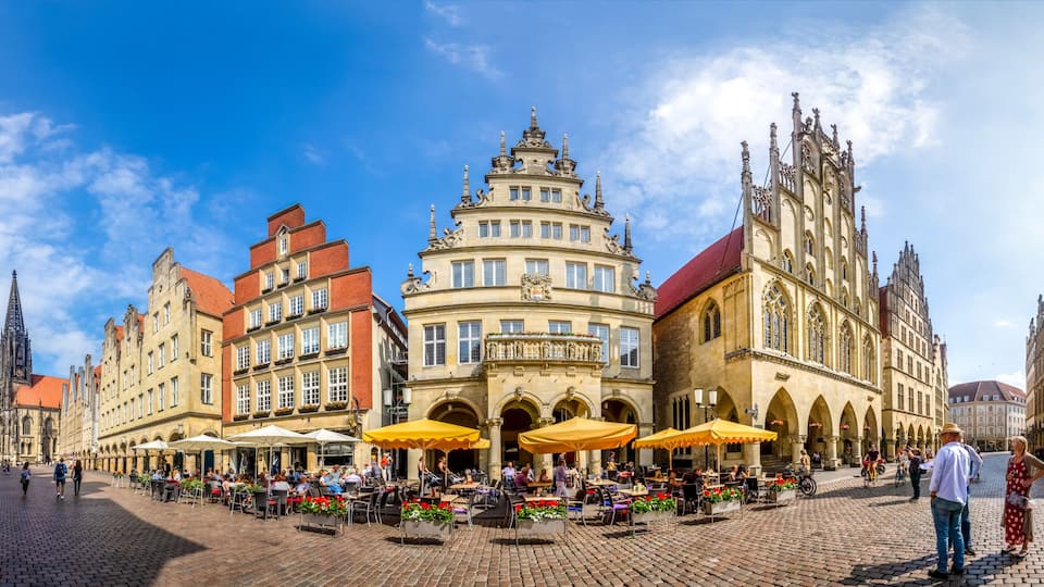 A historic square with ornate buildings, outdoor cafes, and a prominent church spire.