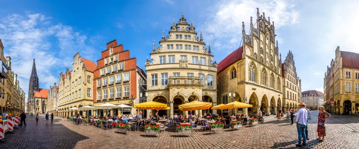 A historic square with ornate buildings, outdoor cafes, and a prominent church spire.