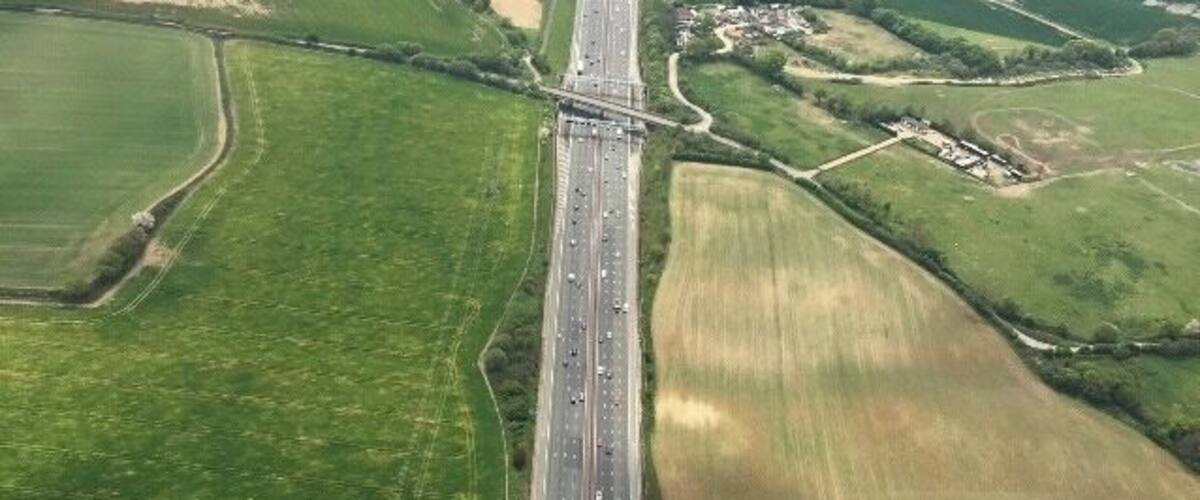 An aerial view of a highway with surrounding agricultural fields and a small settlement.