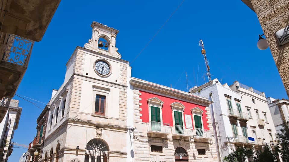 A historic building with a clock tower, red facade, and green shutters.