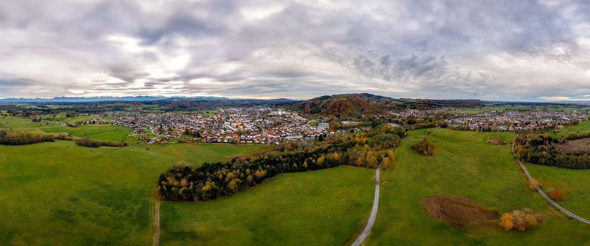 A panoramic view of a town surrounded by green fields and a mountain range.