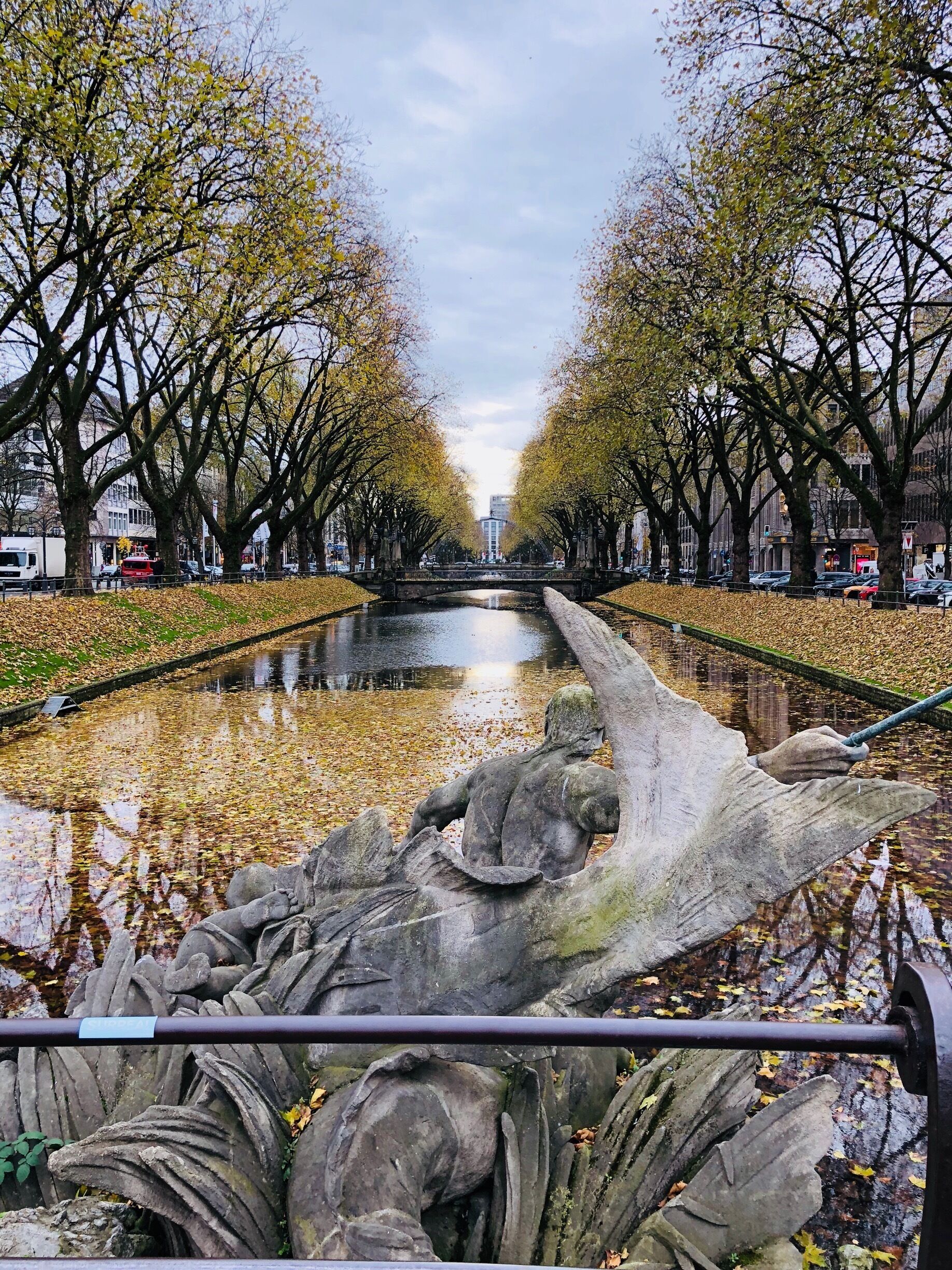 Un canal bordeado por árboles cubiertos de hojas y una escultura de piedra.