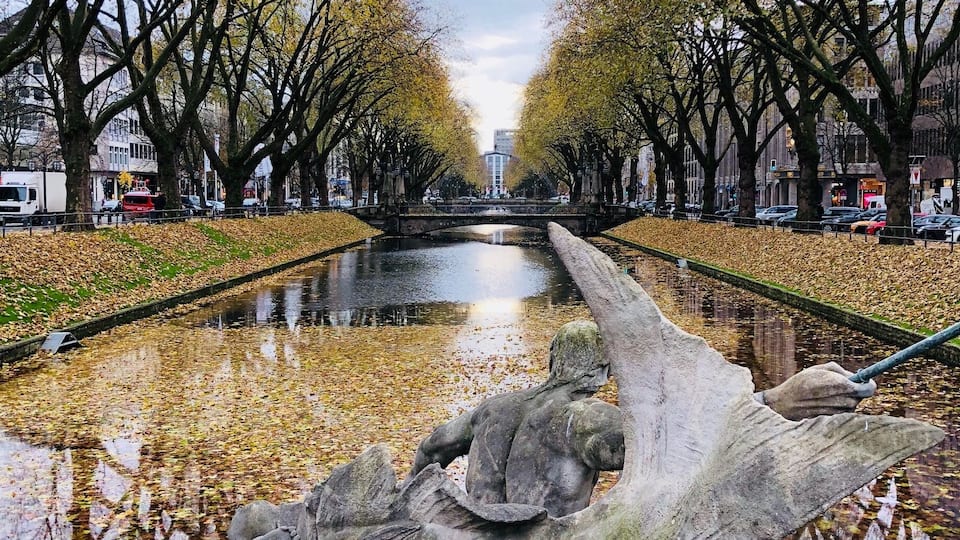 Un canal bordeado por árboles cubiertos de hojas y una escultura de piedra.