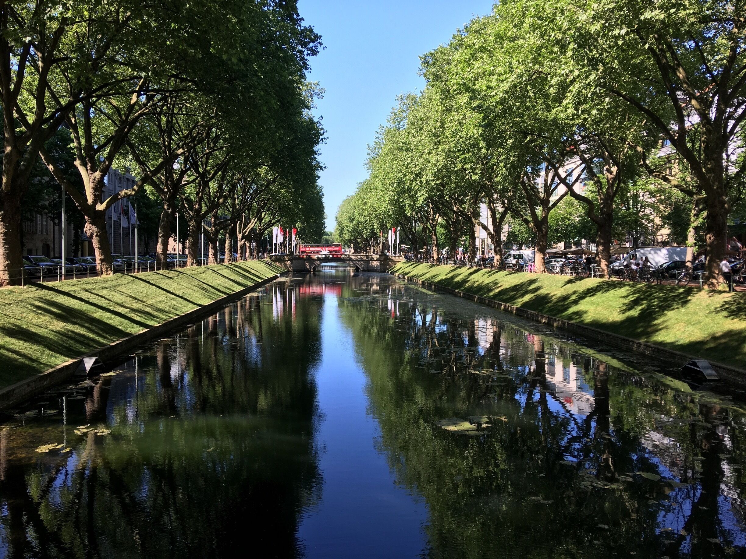 Een kanaal met bomen en een rode brug in de verte.