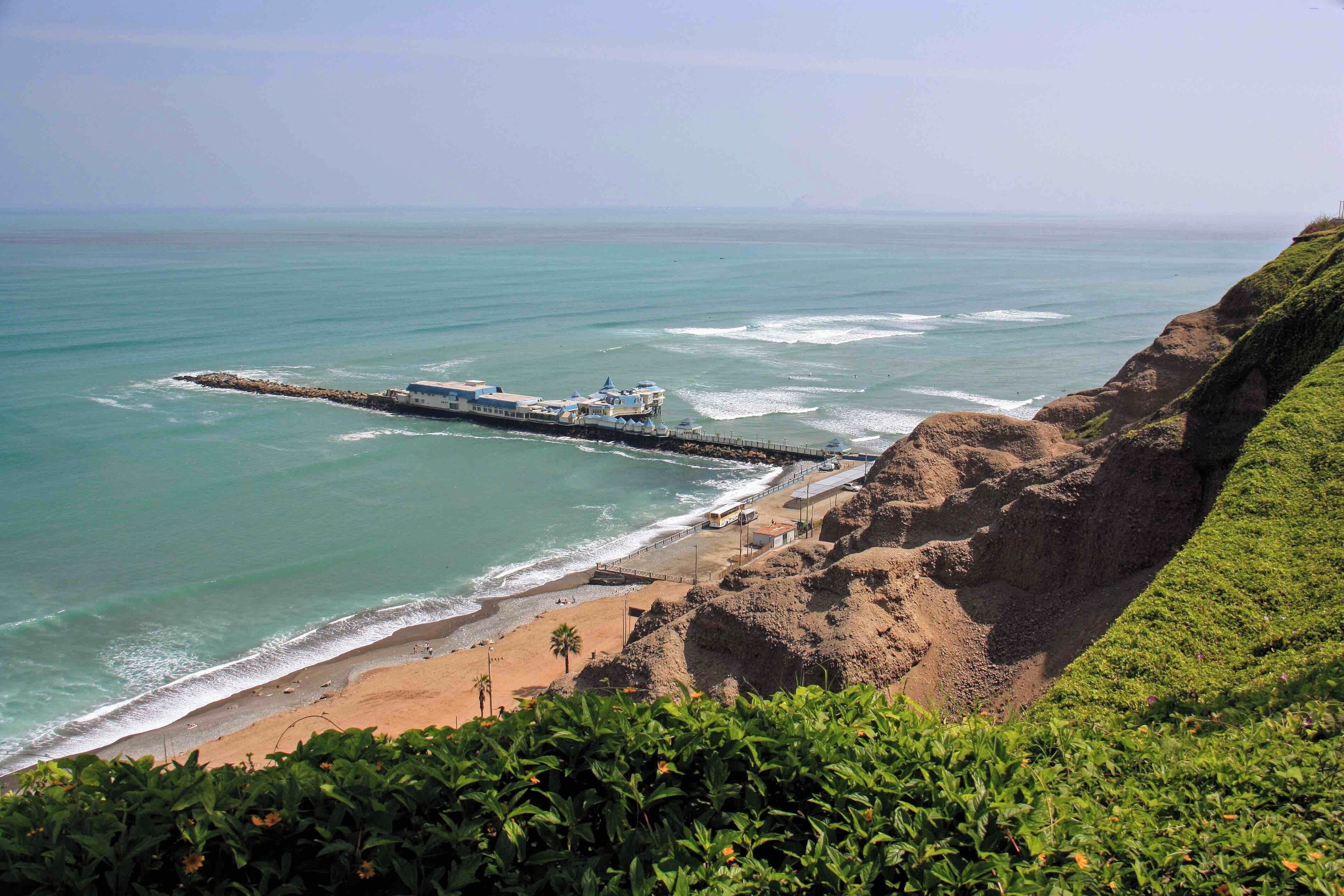 The view of the coast and pier at Miraflores in Lima, Peru. There is a very nice paved walkway along the main avenue that has views over looking the coast and beaches for miles. The walkways pass through some well maintained parks and the popular Larcomar shopping mall. It is also common to see paragliders soaring above the cliffs in this area.