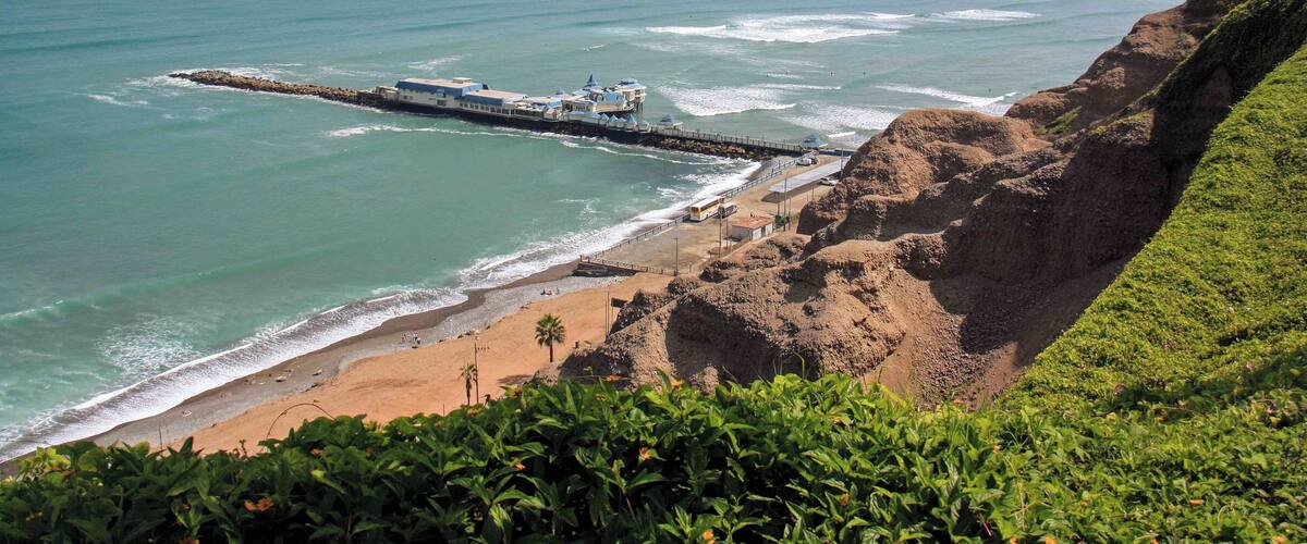 The view of the coast and pier at Miraflores in Lima, Peru. There is a very nice paved walkway along the main avenue that has views over looking the coast and beaches for miles. The walkways pass through some well maintained parks and the popular Larcomar shopping mall. It is also common to see paragliders soaring above the cliffs in this area.