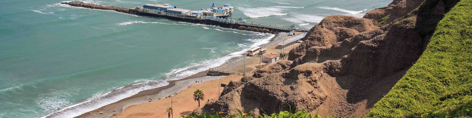 The view of the coast and pier at Miraflores in Lima, Peru. There is a very nice paved walkway along the main avenue that has views over looking the coast and beaches for miles. The walkways pass through some well maintained parks and the popular Larcomar shopping mall. It is also common to see paragliders soaring above the cliffs in this area.