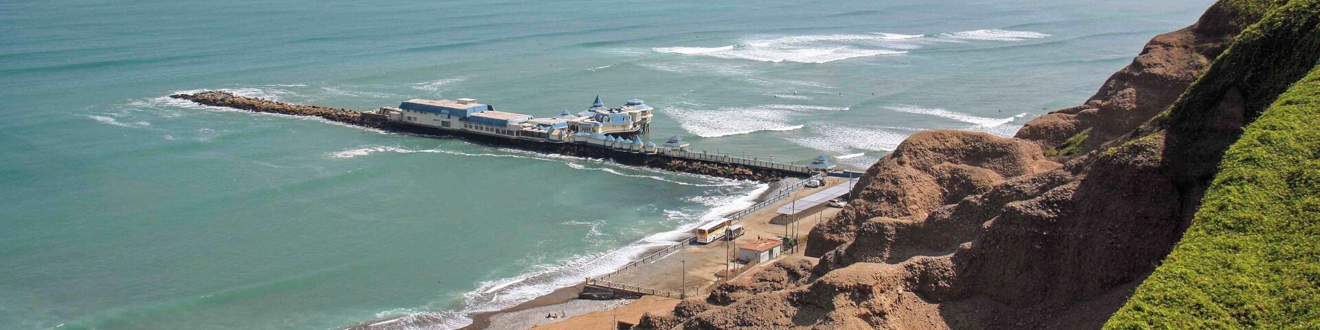 The view of the coast and pier at Miraflores in Lima, Peru. There is a very nice paved walkway along the main avenue that has views over looking the coast and beaches for miles. The walkways pass through some well maintained parks and the popular Larcomar shopping mall. It is also common to see paragliders soaring above the cliffs in this area.