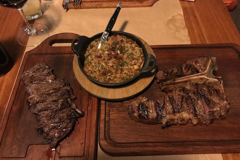 Une table en bois avec un bol de soupe, deux steaks et un verre de vin rouge.
