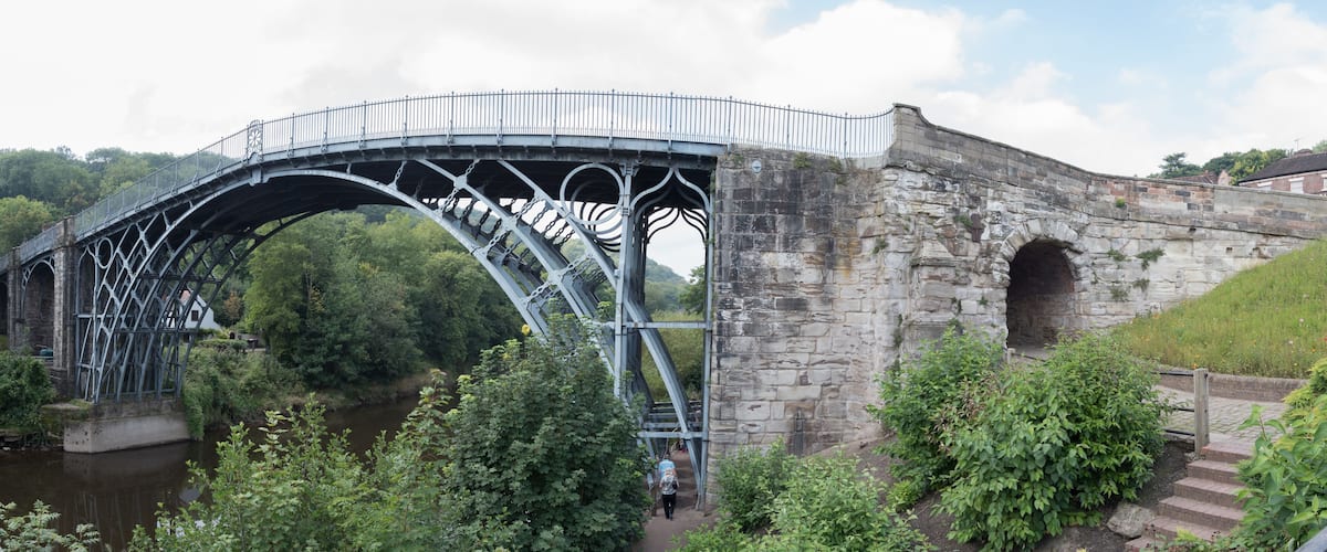 A stone bridge with a metal arch and a stone building in the background.