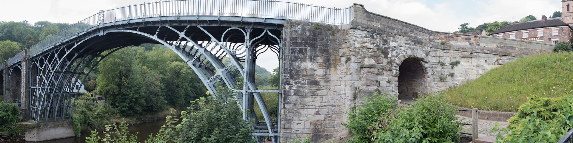 A stone bridge with a metal arch and a stone building in the background.