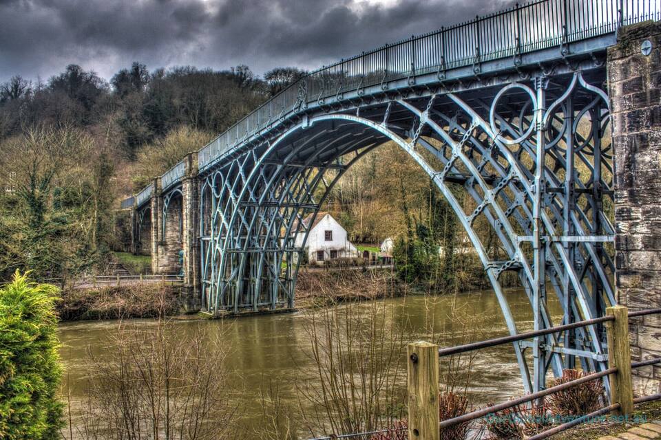 A blue metal bridge over a river with a white house in the background.