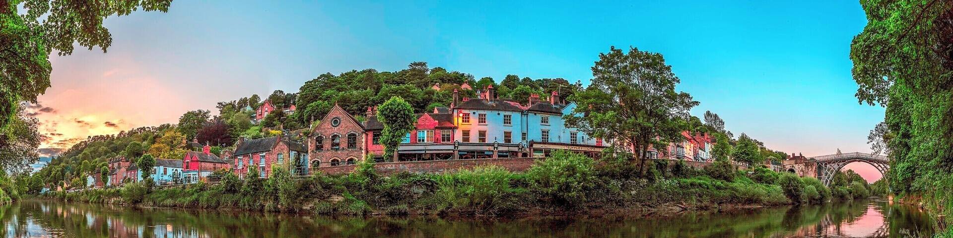 A riverside town with colorful buildings, a bridge, and lush greenery.